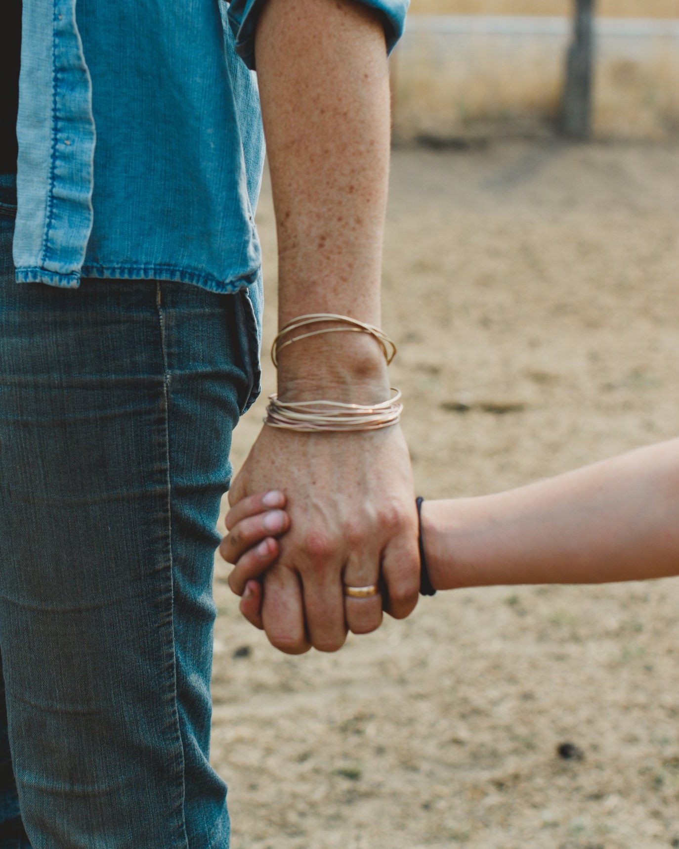 An adult in a denim shirt holding a child's hand on the ranch