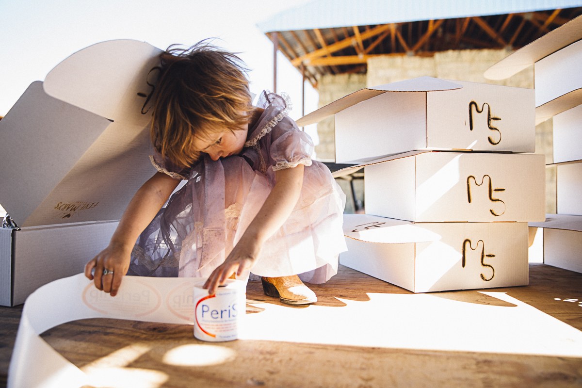 A little girl in a dress helping with shipping labels next to a stack of M5 branded boxes