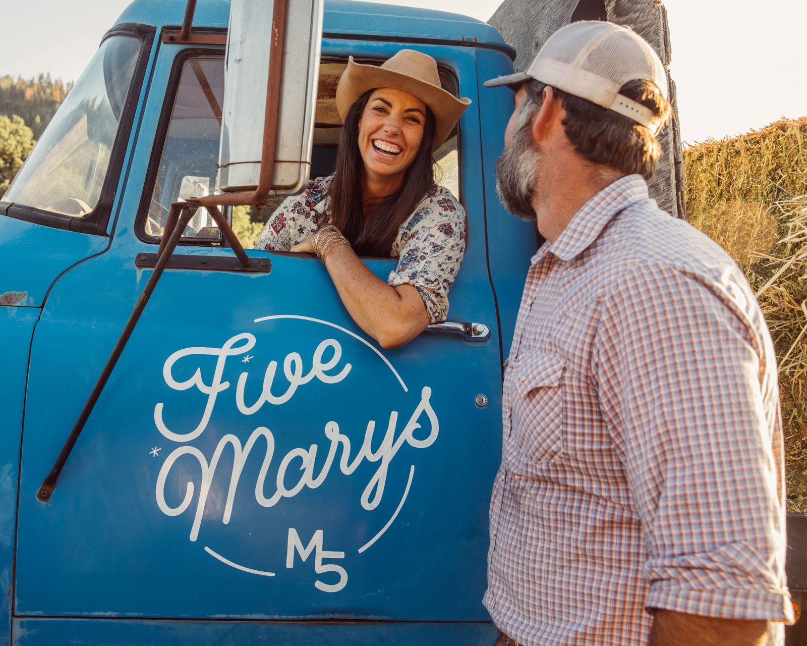 Mary laughing from the window of the blue Five Marys hay truck while Brian stands alongside
