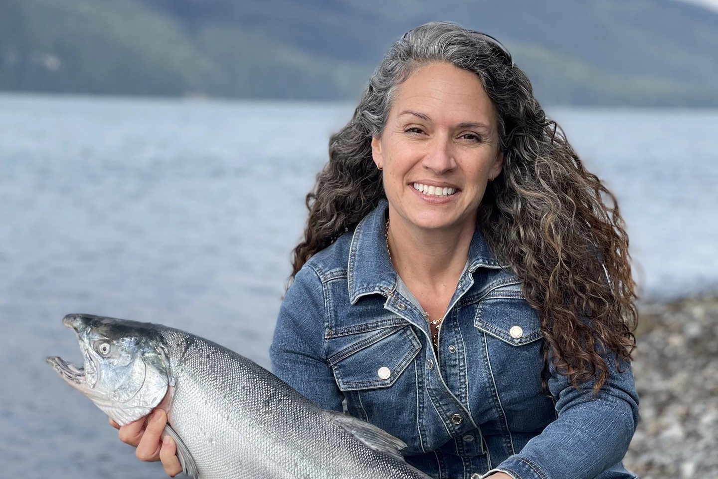 Sarah Ecolano of Copper River Fish Market holding a salmon on the shore in Alaska