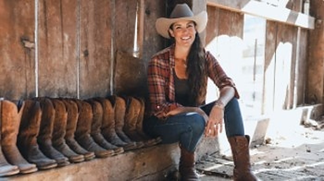 Mary sitting on a barn porch next to a long row of cowboy boots