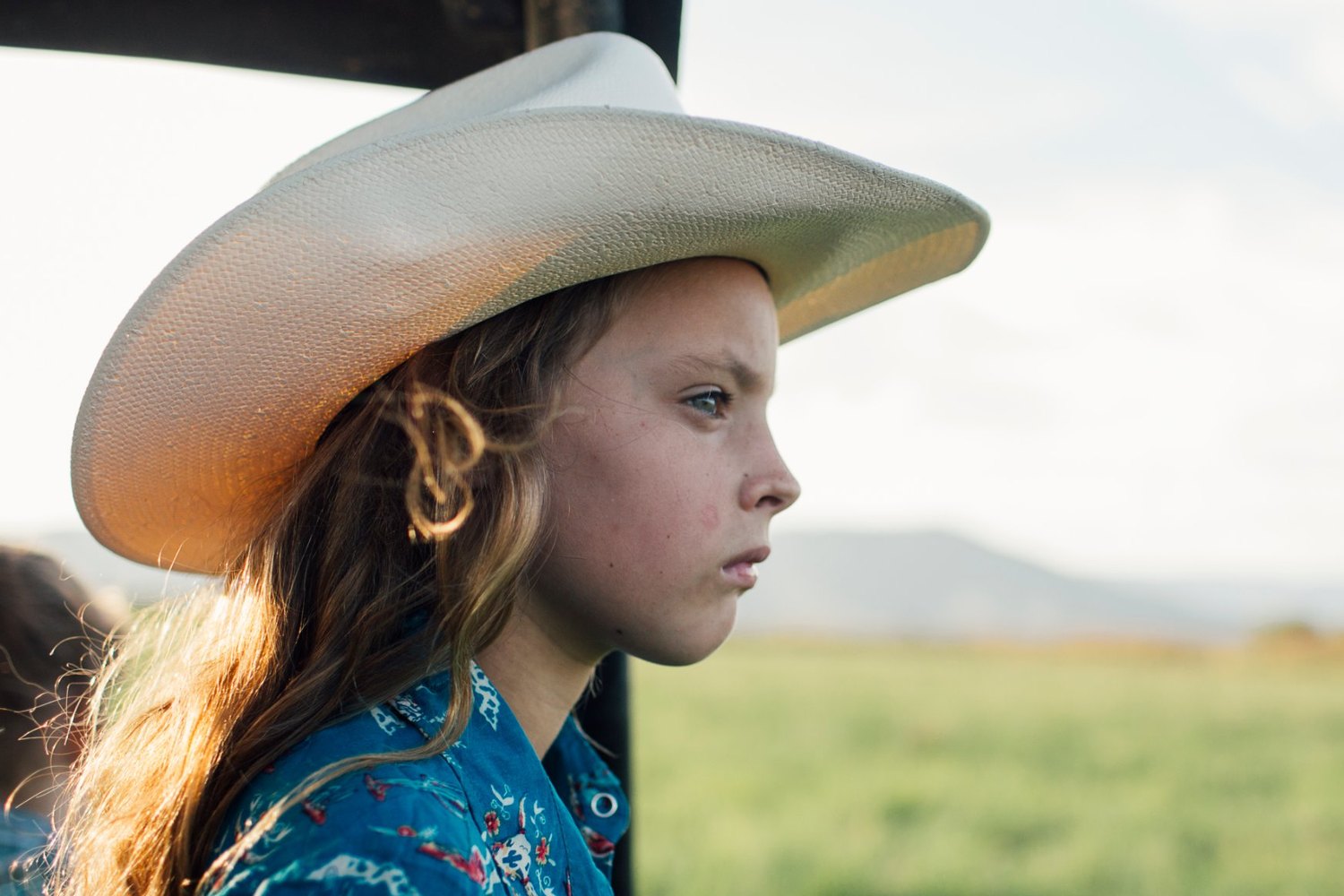 A young cowgirl in a straw hat looking out over a green pasture at Five Marys Ranch