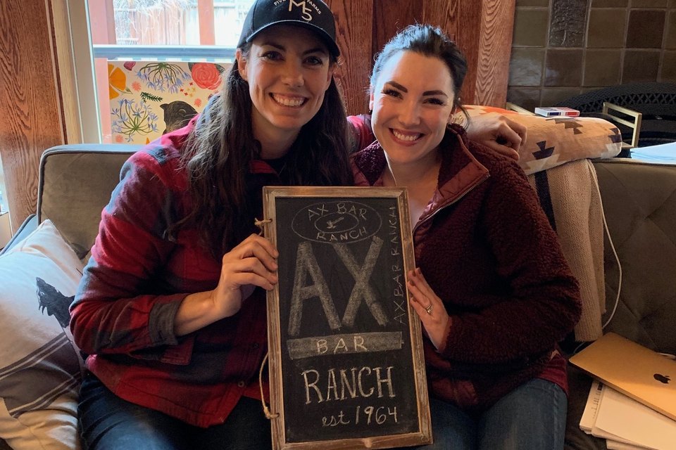 Mary Heffernan and Wendy Axtell holding the AX Bar Ranch chalkboard sign