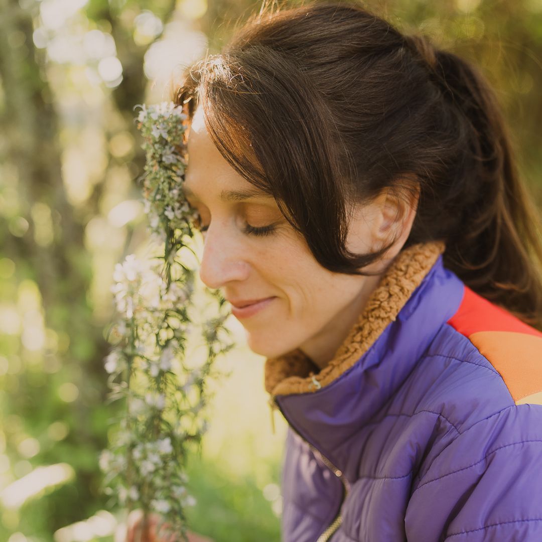 Amelia in profile, eyes closed, face turned toward a sprig of rosemary in bloom, soft golden light, dreamy and close 