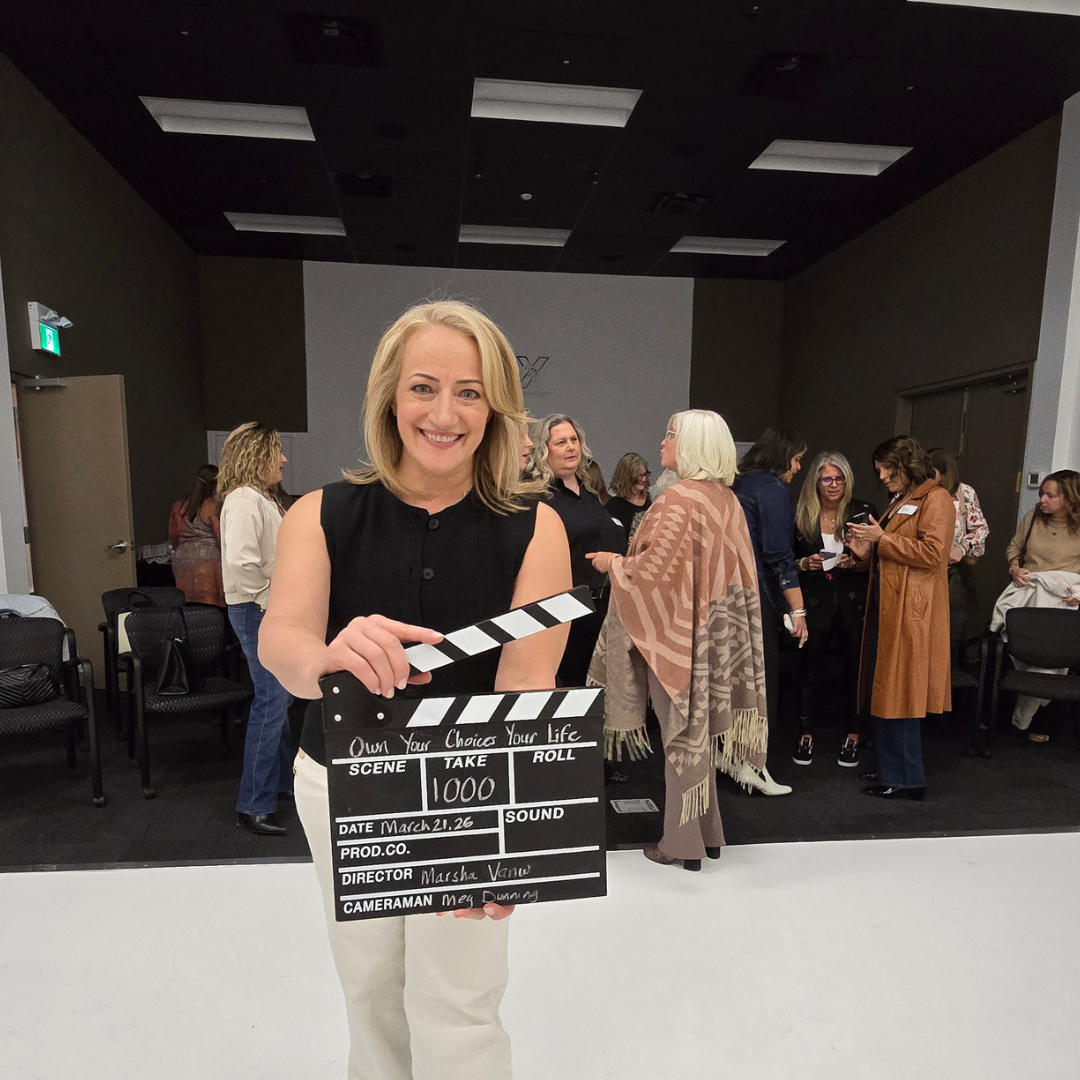 Marsha holding a film clapperboard at a live event while attendees mingle behind her