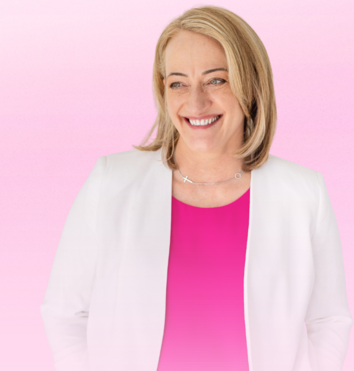 Marsha smiling in a white blazer and pink top against a pink background