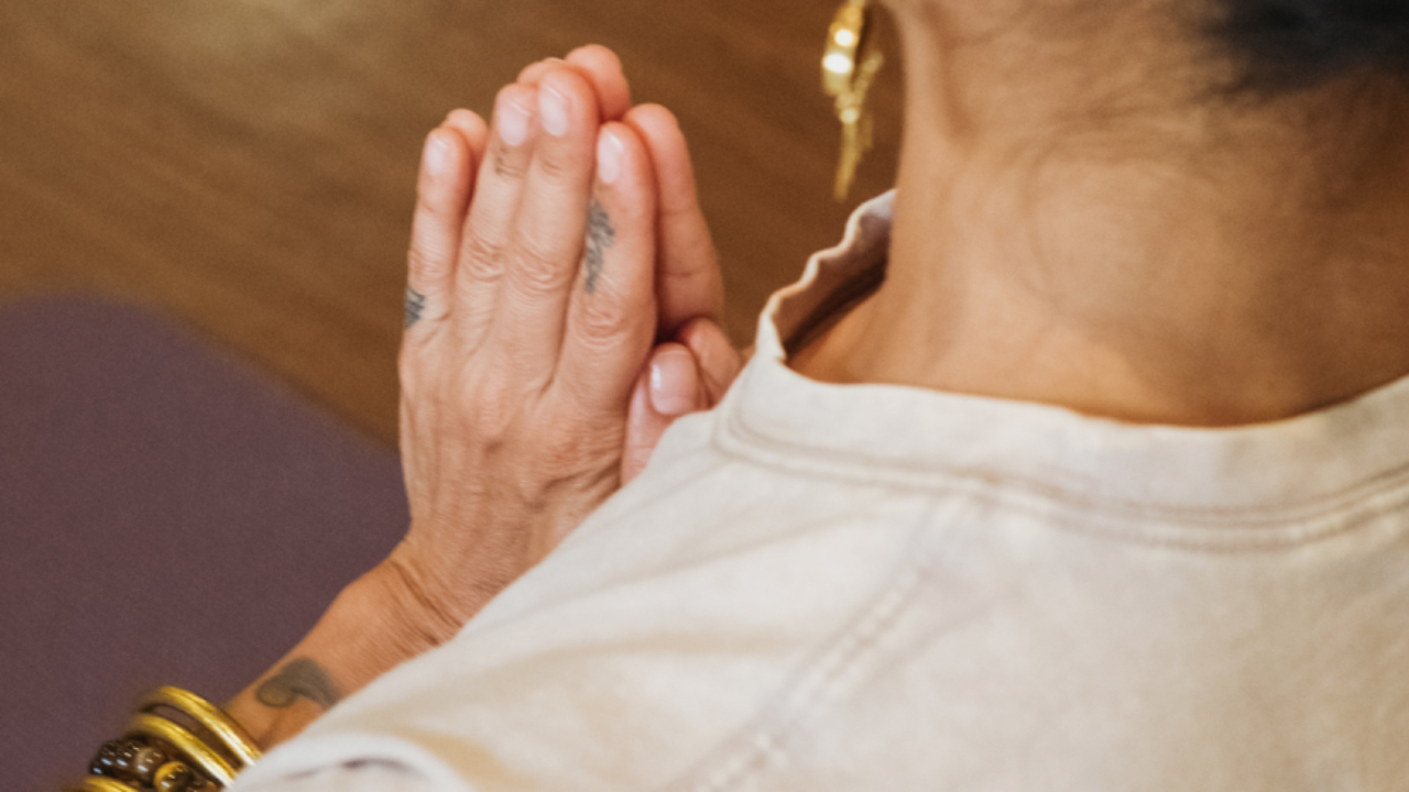 Woman holding hands in prayer position with finger tattoos and gold bracelet.