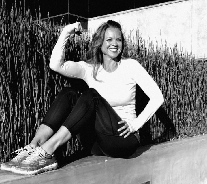 Alicia sitting on a ledge, flexing and smiling
