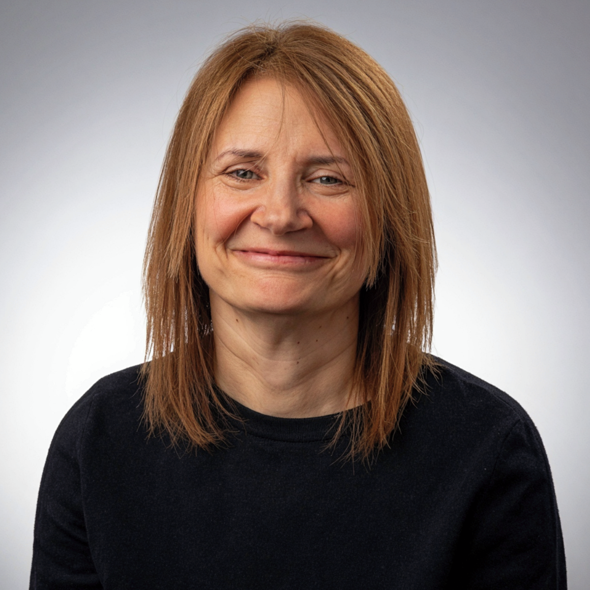 Picture of Kate smiling with a black roundneck top on, grey background.