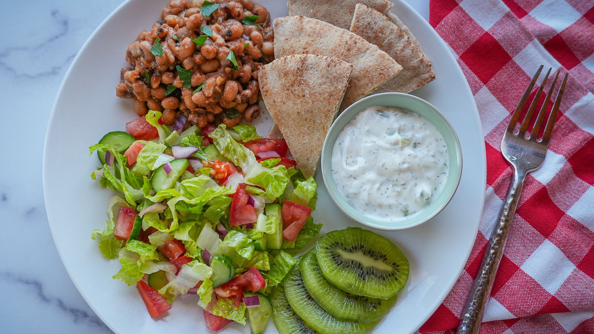 Healthy Greek black-eyed peas meal with cucumber salad, whole wheat pita, and tzatziki sauce.