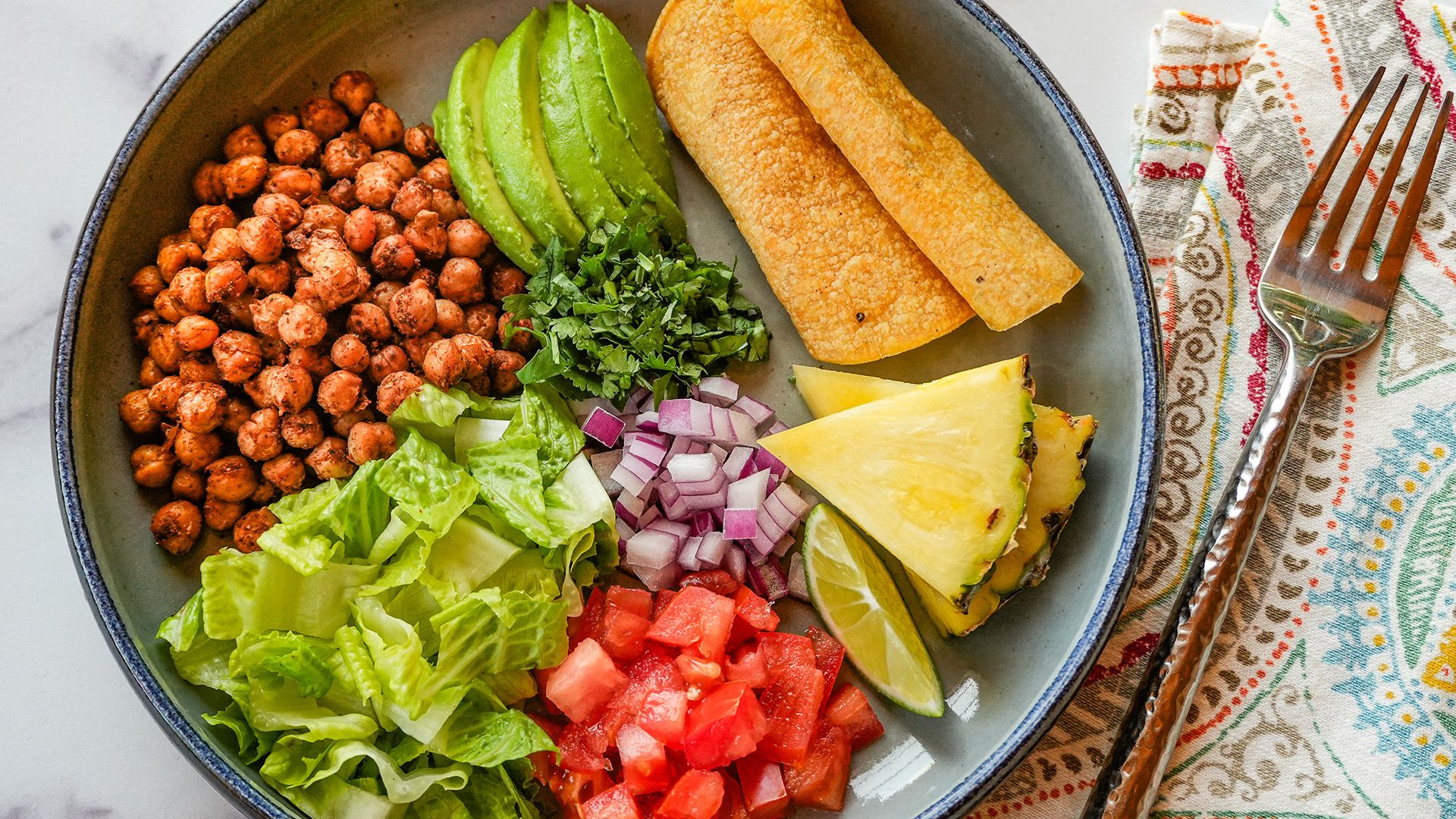 A colorful bowl of taco ingredients featuring black beans, diced tomatoes, fresh greens, and yellow corn tortillas.
