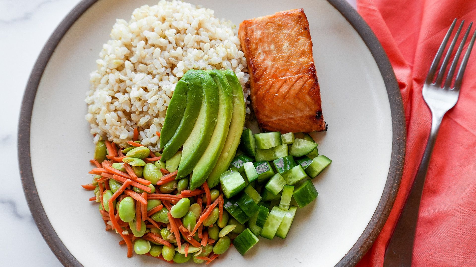 A plated meal featuring miso glazed salmon, cooked brown rice, edamame stir-fry, and sliced avocado.