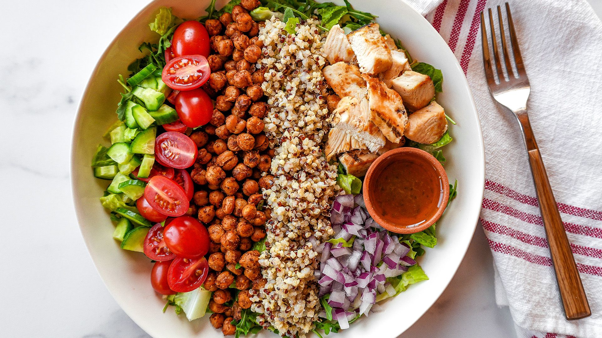 A vibrant Mediterranean salad bowl featuring grilled chicken, seasoned chickpeas, quinoa, fresh cherry tomatoes, cucumbers, and mixed greens.