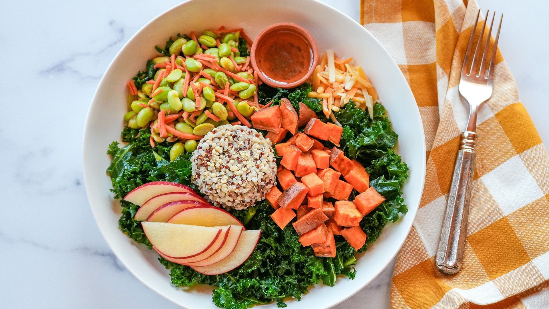 Kale Edamame Crunch Salad topped with roasted sweet potatoes, quinoa, and sliced apples.