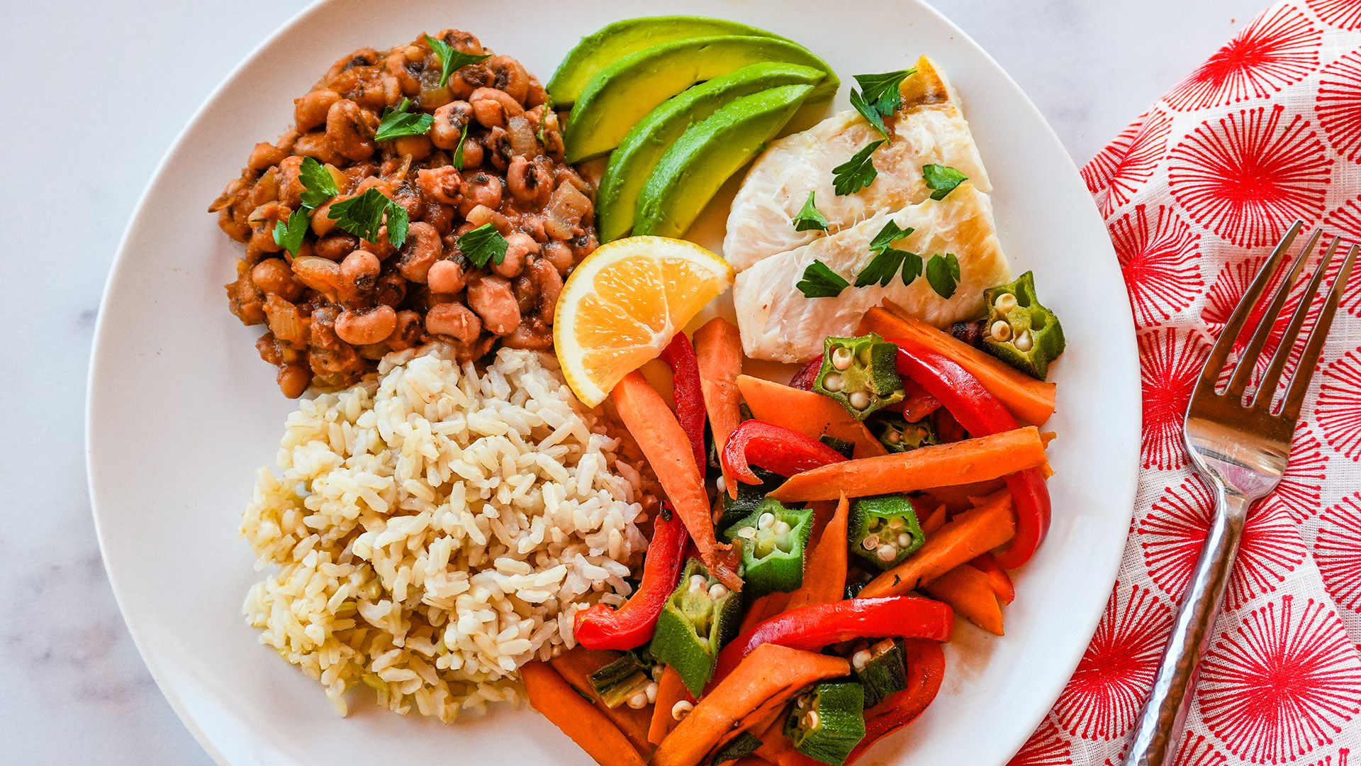 Caribbean black-eyed peas with grilled fish, brown rice, avocado, and sauteed vegetables on a plate.