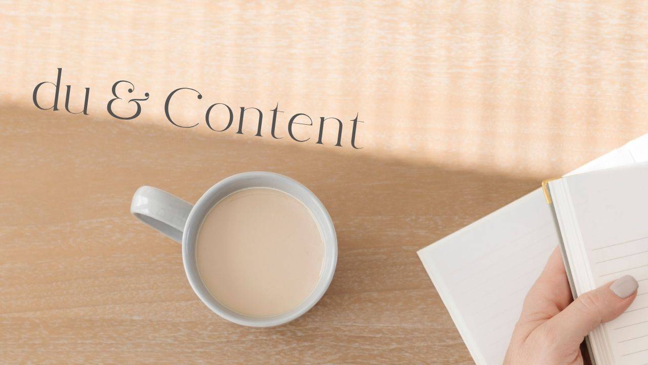 kaffee und buch in der Hand von einer Frau auf einem holzfarbenen tisch
