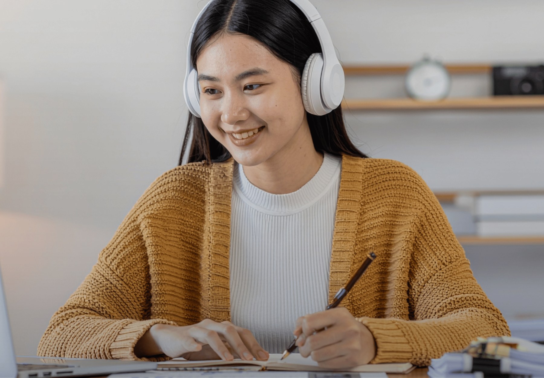 Woman wearing headphones taking notes beside her laptop