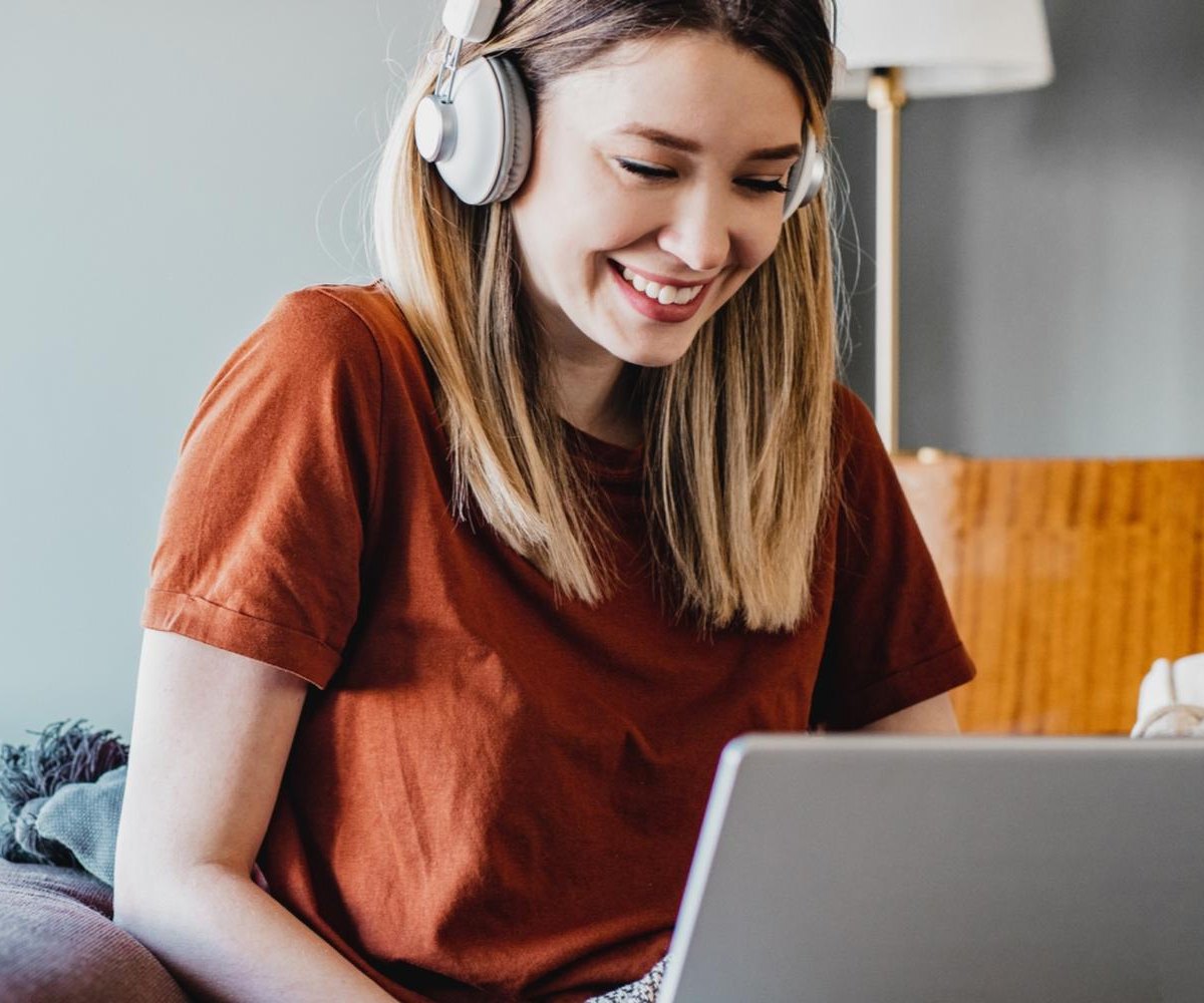 Smiling woman wearing headphones, learning transcription on a laptop at home