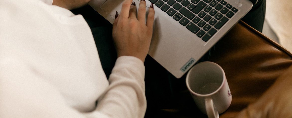 Hands typing on a laptop at home with a mug of coffee