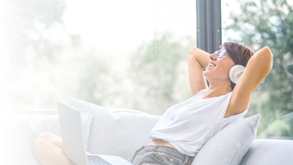 Relaxed woman with headphones and a laptop on a couch at home