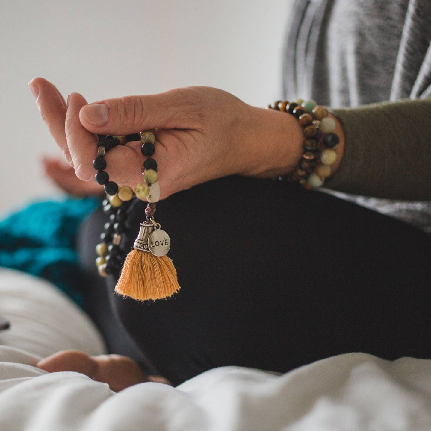 Woman journaling with coffee and mala beads on a black table near a window.