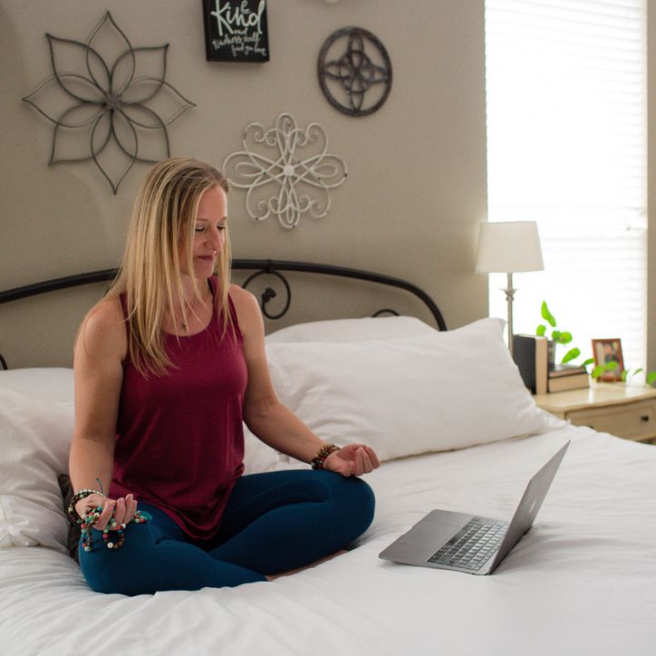 Home yoga setup with a mat, props, and a laptop streaming a virtual class in a cozy living room near a fireplace.