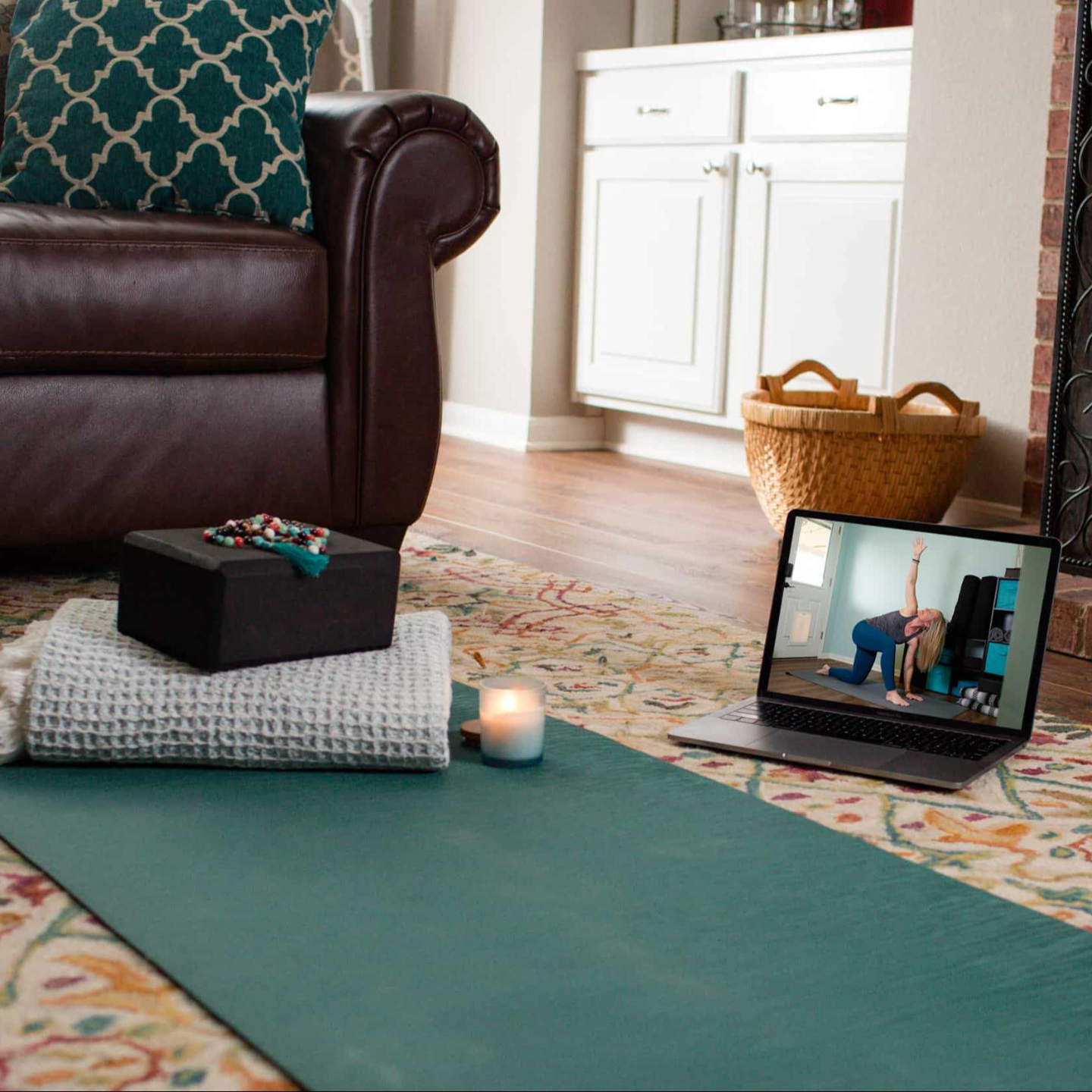 Home yoga setup with a mat, props, and a laptop streaming a virtual class in a cozy living room near a fireplace.