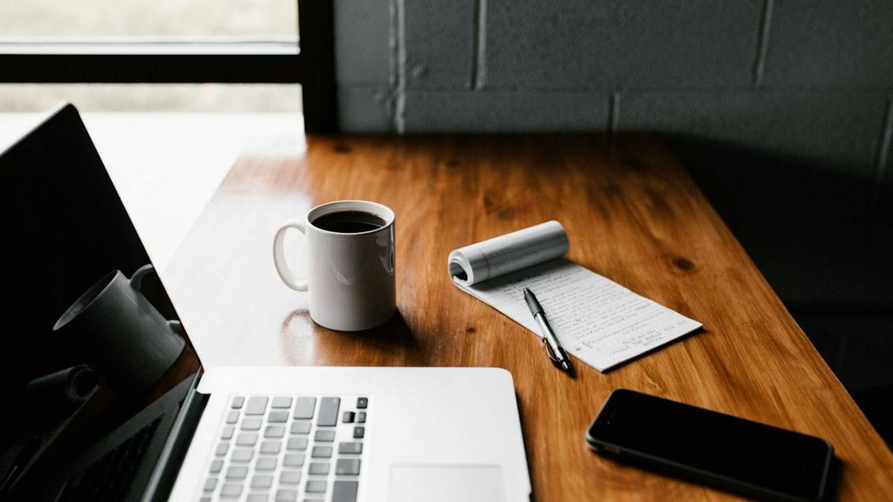 Laptop, cup of coffee, phone and pad of paper on a desk
