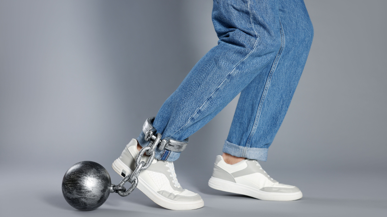 Man with metal ball and chain on his leg against grey background, closeup