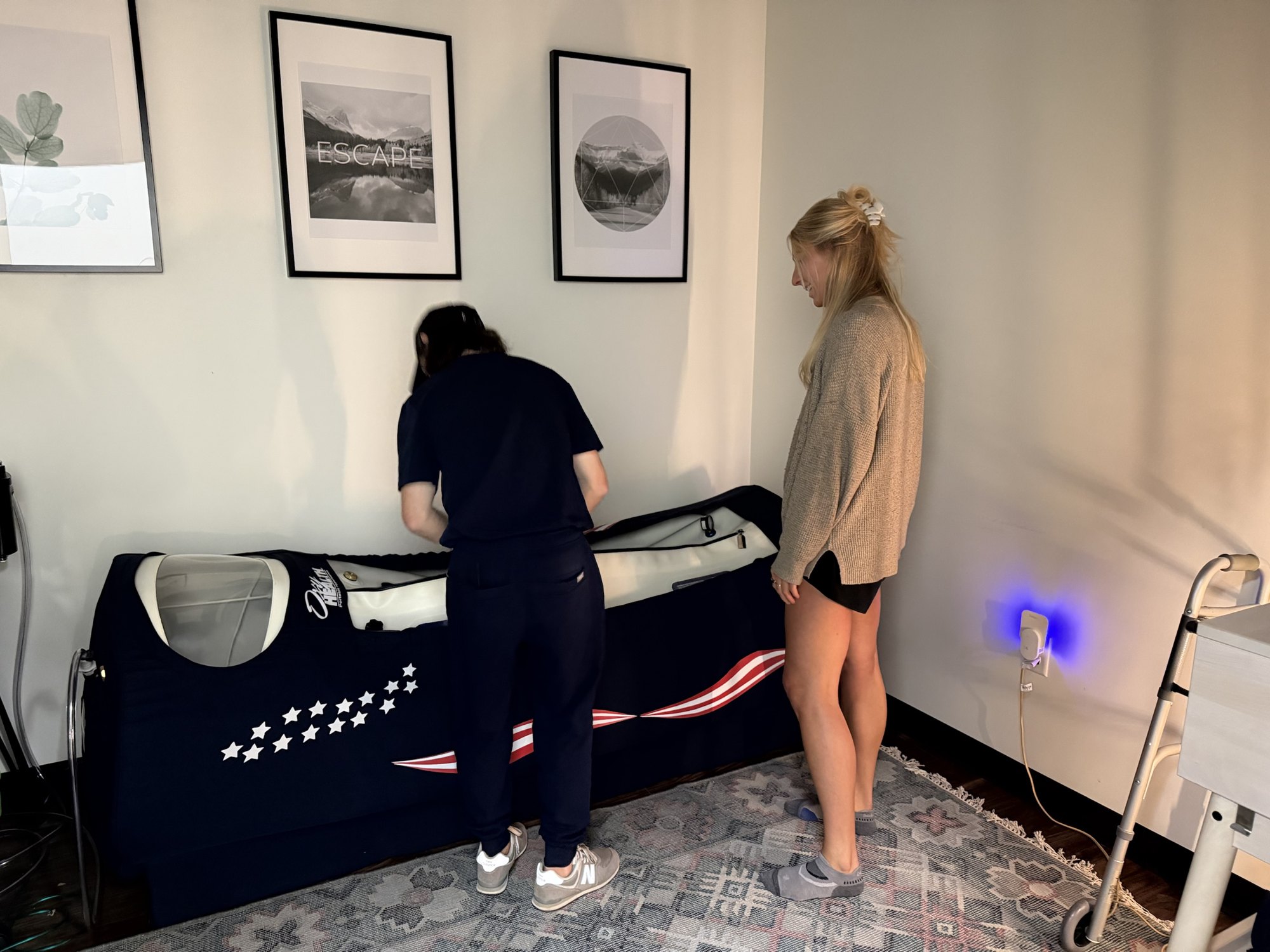 A patient smiling beside the OxyHealth hyperbaric chamber at HBOT Chattanooga