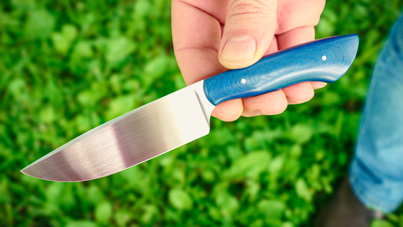 Finished blue-handled hunting knife held outdoors, from Kyle Royer's knifemaking course