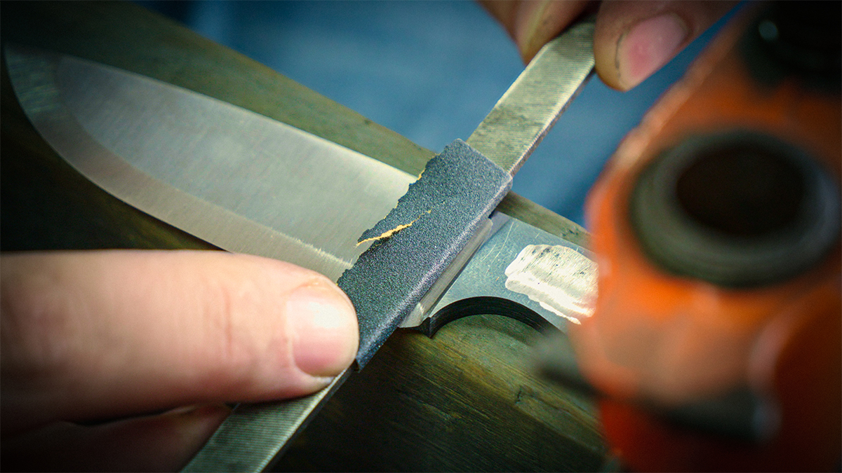 Hand sanding a hunting knife blade during Kyle Royer's step-by-step knifemaking