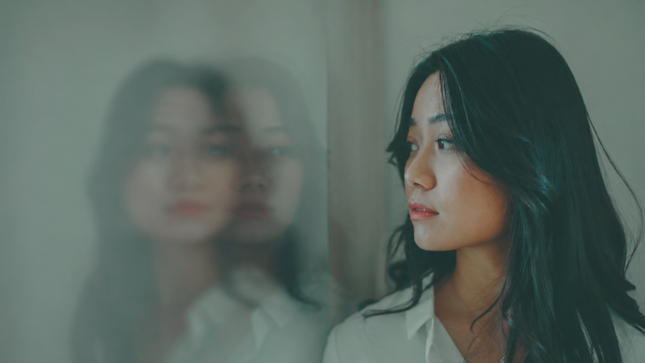 A woman looks into a mirror and her face is blurry, double exposed. Loss of identity concept. 