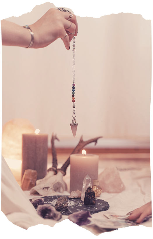 Hand holding a pendulum over crystals and candles for dowsing