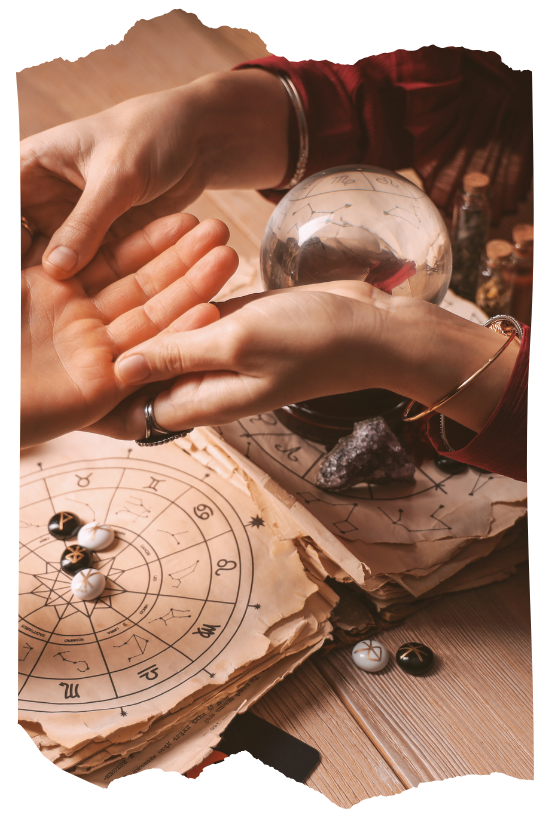 Hands performing a palm reading beside a crystal ball and astrology chart