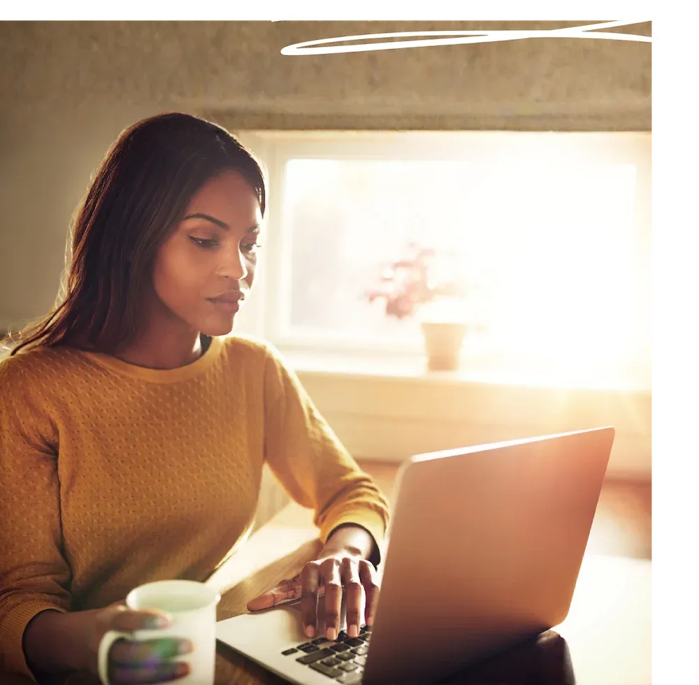 Woman working on laptop with coffee in warm, natural light setting, representing professional website design and online business support services.