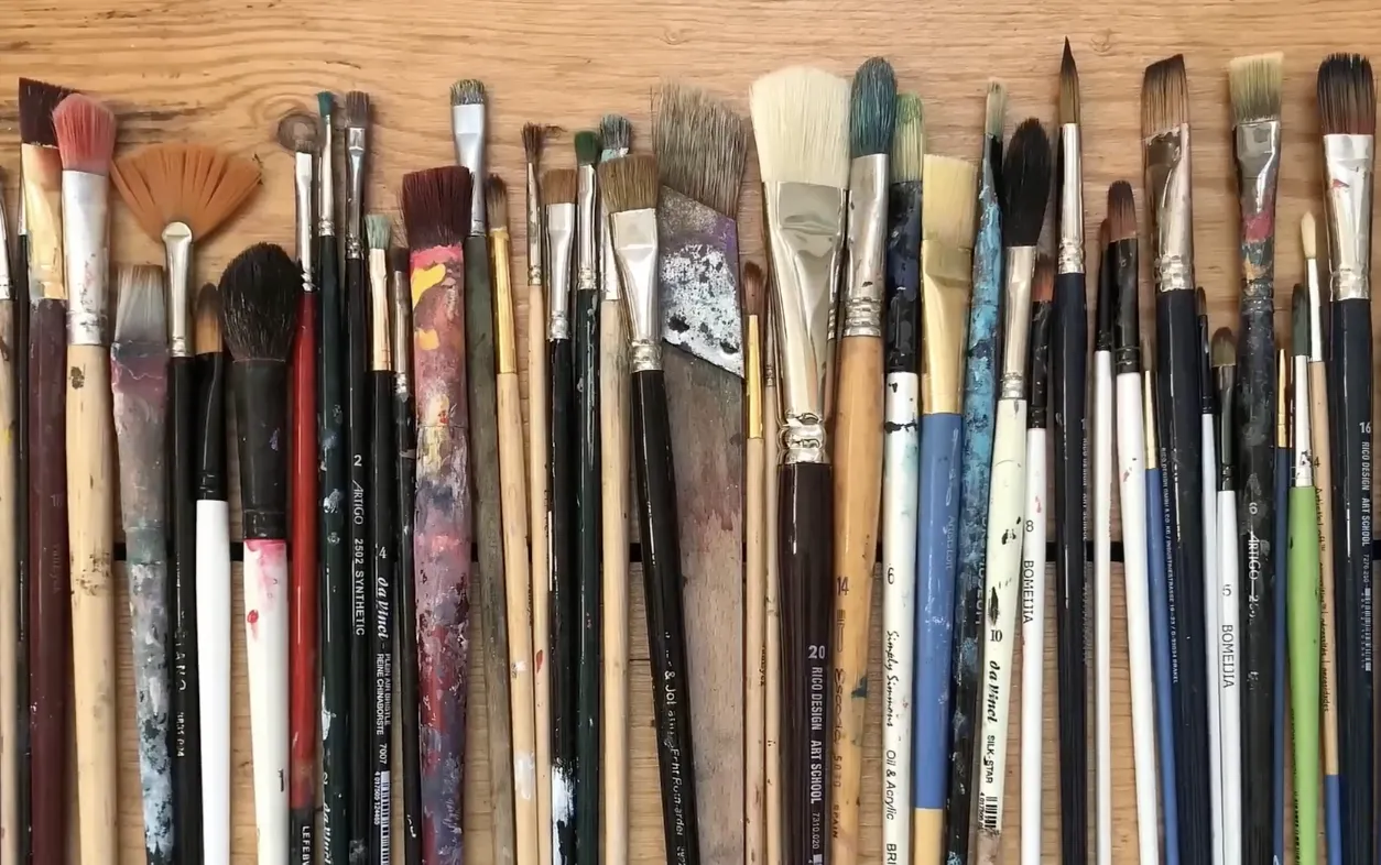 A collection of synthetic acrylic paint brushes laid out on a wooden table