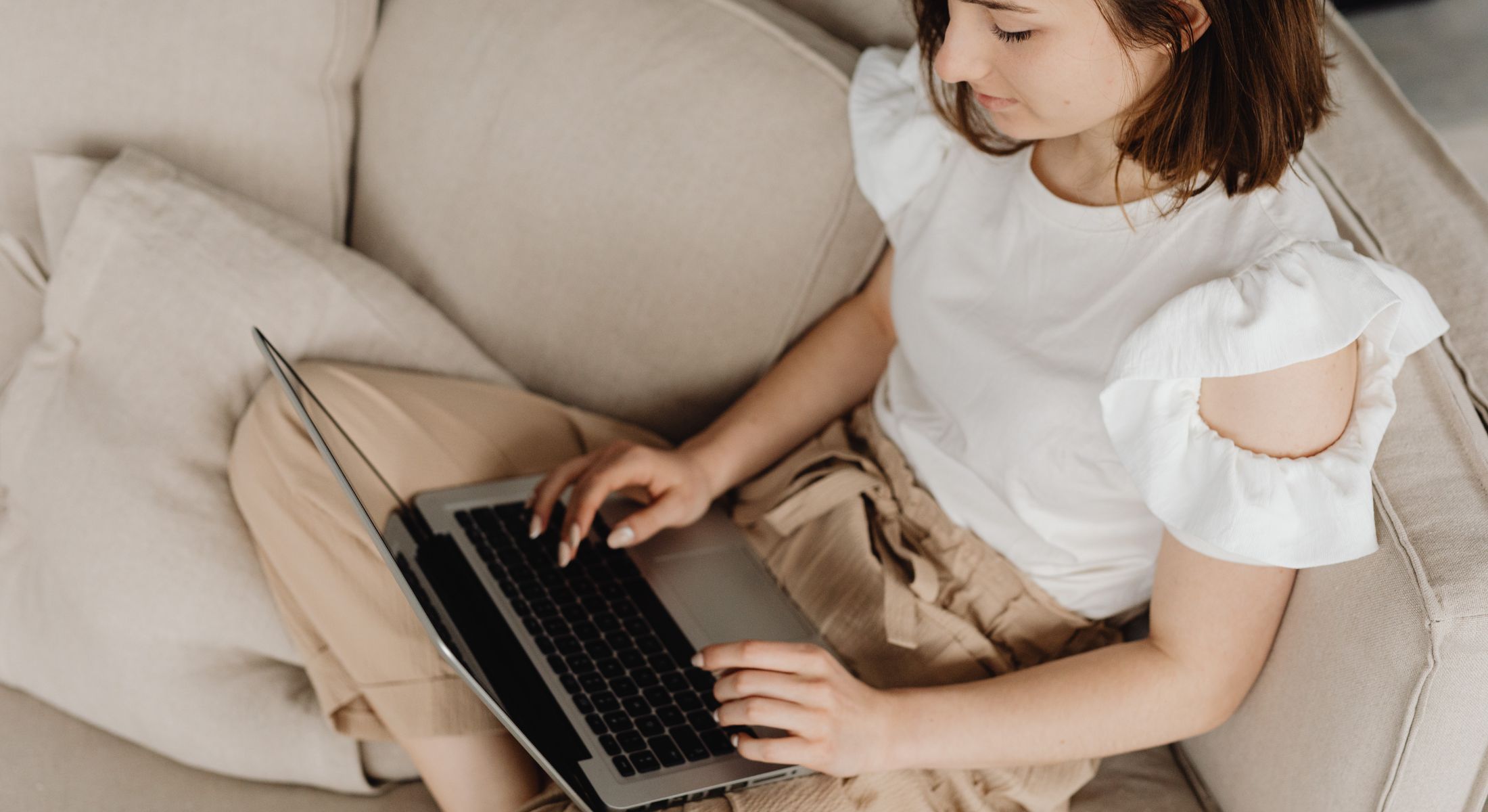 Woman sitting on a beige sofa typing on a laptop