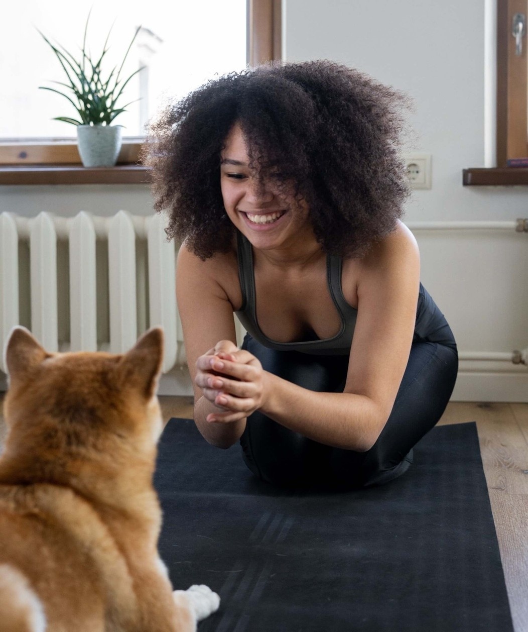 Woman smiling on a yoga mat at home with her dog watching her