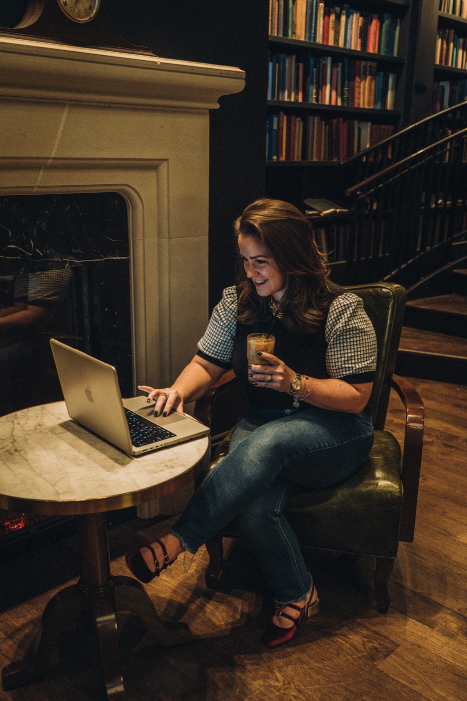 Jordan working on a laptop by a fireplace and bookshelves