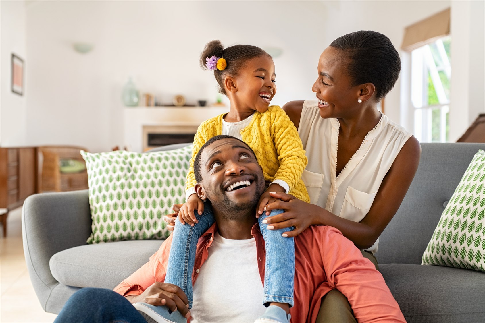 A mother, father, and their young daughter laughing together on the sofa at home