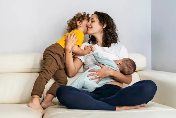 Mother breastfeeding her baby on couch snuggling toddler
