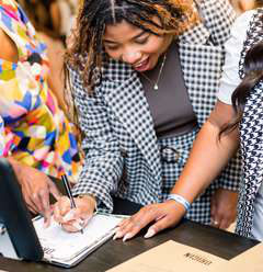 A woman in a checked blazer signing a form at a vendor table.