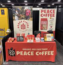 A Peace Coffee vendor table with a red cloth and bags of coffee on display.