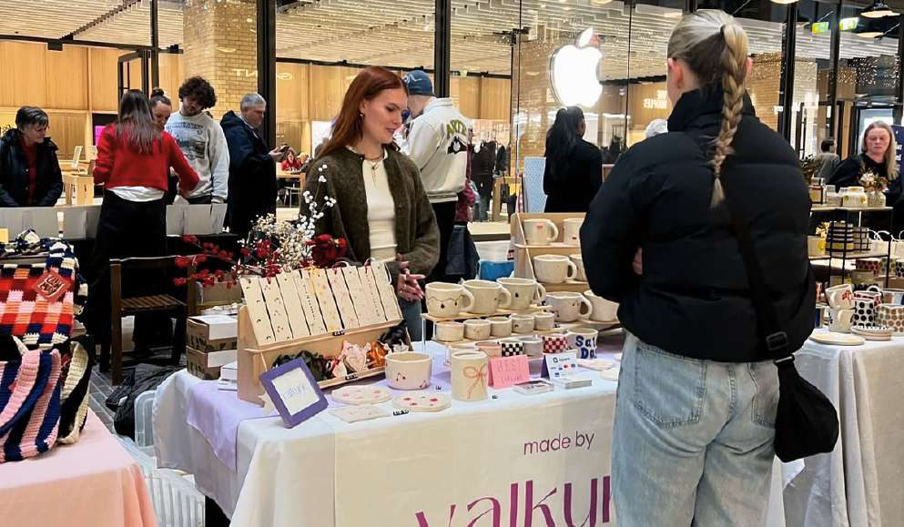 A busy market booth of handmade ceramics with shoppers browsing.