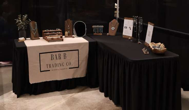 A vendor table dressed with black linens displaying jewellery under a Bar B Trading Co. banner.