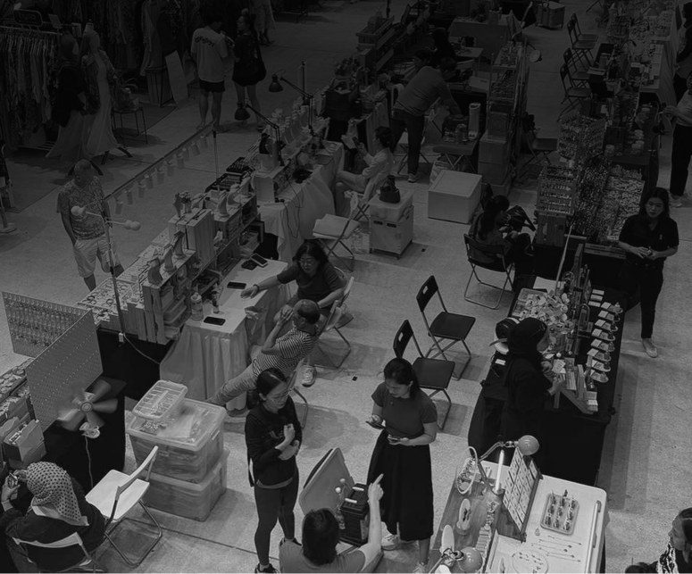 Black-and-white overhead photograph of a busy vendor marketplace full of tables and shoppers.