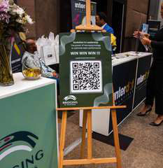 A vendor booth with an easel sign and a QR code beside a white counter.