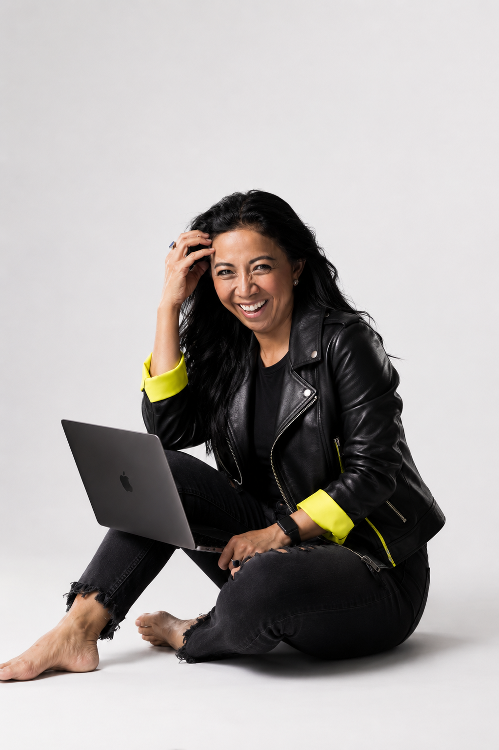 Nim Stant sitting on the floor in a black leather jacket with a laptop open on her knee, laughing.