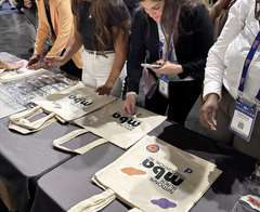 Branded tote bags laid out on a vendor table with attendees nearby.